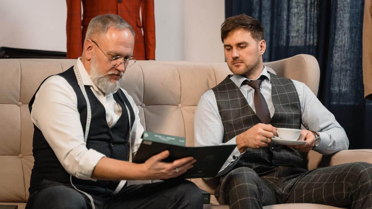Tailor and client reviewing fabric samples for a custom suit in a stylish workshop.